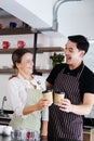Smiling young barista couple loves Asian man and caucasian woman is hugging and holding cups of hot coffee together. Start up