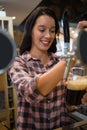 Smiling young barmaid pouring drink from tap in glass Royalty Free Stock Photo