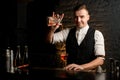 Smiling young bartender at bar pours cocktail into glass