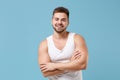 Smiling young bearded guy 20s in white singlet posing isolated on pastel blue wall background studio portrait. Sport