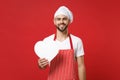 Smiling young bearded male chef cook or baker man in striped apron t-shirt toque chefs hat isolated on red background Royalty Free Stock Photo