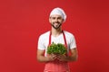 Smiling young bearded male chef cook or baker man in striped apron white t-shirt toque chefs hat isolated on red Royalty Free Stock Photo