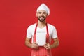 Smiling young bearded male chef cook or baker man in striped apron white t-shirt toque chefs hat isolated on red wall Royalty Free Stock Photo