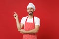 Smiling young bearded male chef cook baker man in striped apron white t-shirt toque chefs hat posing isolated on red Royalty Free Stock Photo