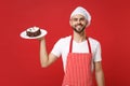 Smiling young bearded male chef cook or baker man in striped apron white t-shirt toque chefs hat posing isolated on red Royalty Free Stock Photo