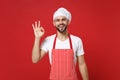 Smiling young bearded male chef cook or baker man in striped apron white t-shirt toque chefs hat posing isolated on red Royalty Free Stock Photo