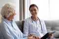 Smiling young beautiful female doctor consulting older patient at home. Royalty Free Stock Photo