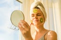 Smiling young beautiful woman close up at home near the window with natural homemade fruit facial mask of kiwi on face, towel on Royalty Free Stock Photo