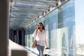 Smiling young biracial businesswoman talking on phone walking with luggage at airport corridor Royalty Free Stock Photo