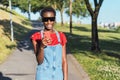 Smiling young black African woman fashion model chatting on her cell phone walking in a park wearing sunglasses. Royalty Free Stock Photo