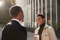 Smiling young black businesswoman standing on the street with a takeaway coffee, talking to her male colleague, selective focus Royalty Free Stock Photo