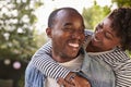 Smiling young black couple piggyback in garden, eyes closed Royalty Free Stock Photo