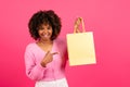 Smiling young black curly woman shopaholic in casual with braces pointing finger at package with purchases Royalty Free Stock Photo