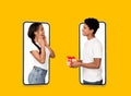 Smiling young black guy gives gift to surprised woman on blank screens of large phone isolated on orange background