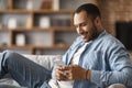 Smiling Young Black Man Using Smartphone While Resting On Couch At Home Royalty Free Stock Photo