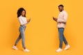 Black man and woman texting on phones and walking on yellow background