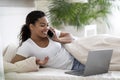 Smiling young black woman with cellphone and laptop relaxing in bed Royalty Free Stock Photo