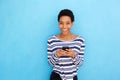 Smiling young black woman holding cellphone by blue background