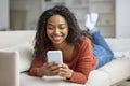 Smiling young black woman texting on smartphone while relaxing at home Royalty Free Stock Photo