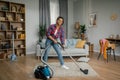 Smiling young black woman with vacuum cleaner dusts floor, enjoy cleaning alone in living room interior