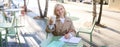 Smiling young blond woman, enjoying her coffee, drinking takeaway and sitting in street cafe, working on project Royalty Free Stock Photo