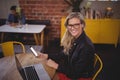 Smiling young blond woman holding smartphone while sitting with laptop at coffee shop Royalty Free Stock Photo