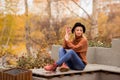 Smiling young blonde in a brown warm sweater, black felt hat, blue jeans and boots sits on a bench in the autumn in the park, Royalty Free Stock Photo