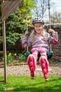 A smiling young blonde girl wearing roller blades and helmet while swinging on a garden swing Royalty Free Stock Photo