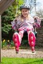 A smiling young blonde girl wearing roller blades and helmet while swinging on garden swing Royalty Free Stock Photo