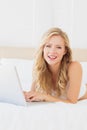 Smiling young blonde lying on her bed using laptop Royalty Free Stock Photo