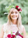 Smiling young blonde in red wreathe stands in the forest