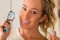 Smiling young blonde woman holding contact lens case on hand and holding in her other hand a blue glasses on blurred Royalty Free Stock Photo