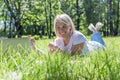 A smiling young blonde woman lies on the grass in a park with a laptop on a summer sunny day. Blogging, online communication, Royalty Free Stock Photo