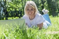 A smiling young blonde woman lies on the grass in a park with a laptop on a summer sunny day. Blogging, online communication, Royalty Free Stock Photo