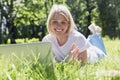 A smiling young blonde woman lies with a laptop on the grass in a park on a sunny summer day. Blogging, online communication and Royalty Free Stock Photo