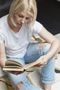 A smiling young blonde woman is sitting with a pile of books and reading. Education and training. Vertical Royalty Free Stock Photo