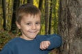 Smiling Young Boy Posing by Tree. Boy posing leaning against a tree in the woods. Royalty Free Stock Photo