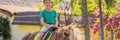 Smiling, young boy ride a pony horse. Horseback riding in a tropical garden BANNER, LONG FORMAT Royalty Free Stock Photo