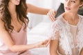 Smiling young bridesmaid helping the bride with her dress