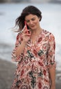 Smiling young brunette caucasian woman chatting on a red mobile phone in the beach. People lifestyle concept Royalty Free Stock Photo