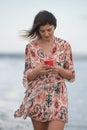 Smiling young brunette caucasian woman chatting on a red mobile phone in the beach. People lifestyle concept Royalty Free Stock Photo