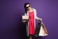 Smiling young brunette lady, in red dress and sunglasses, with shopping bags in her hands