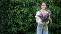 Smiling young brunette woman with a bouquet of flowers near a green wall of bushes. Copy space