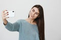 Smiling young brunette woman with long hair making selfie using smart phone. Girl in blue sweater taking photograph with