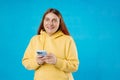 Smiling young brunette woman with smart phone posing isolated on blue background, studio portrait. Cute beautiful young Royalty Free Stock Photo