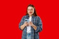 Smiling young brunette woman with smart phone posing isolated on red background, studio portrait. Cute beautiful young Royalty Free Stock Photo