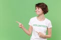Smiling young brunette woman in white volunteer t-shirt isolated on pastel green background in studio. Voluntary free