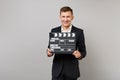 Smiling young business man in classic black suit, shirt holding classic black film making clapperboard isolated on grey Royalty Free Stock Photo