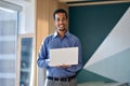 Smiling young business man standing in office with laptop, portrait. Royalty Free Stock Photo