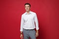 Smiling young business man in white shirt, gray pants posing isolated on bright red wall background studio portrait Royalty Free Stock Photo